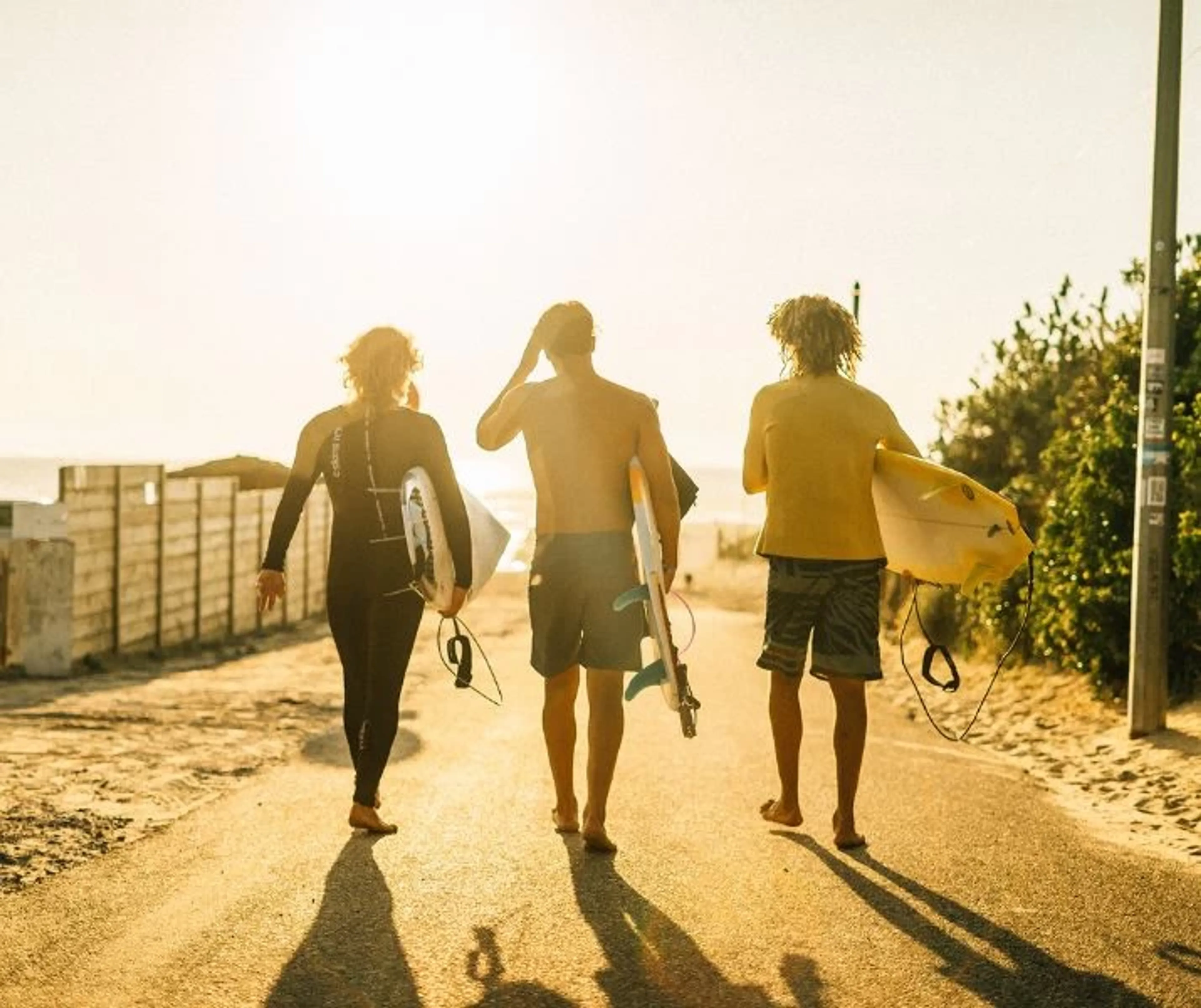 Drei Surfer laufen mit ihren Surfboards vom Surfcamp an den Strand