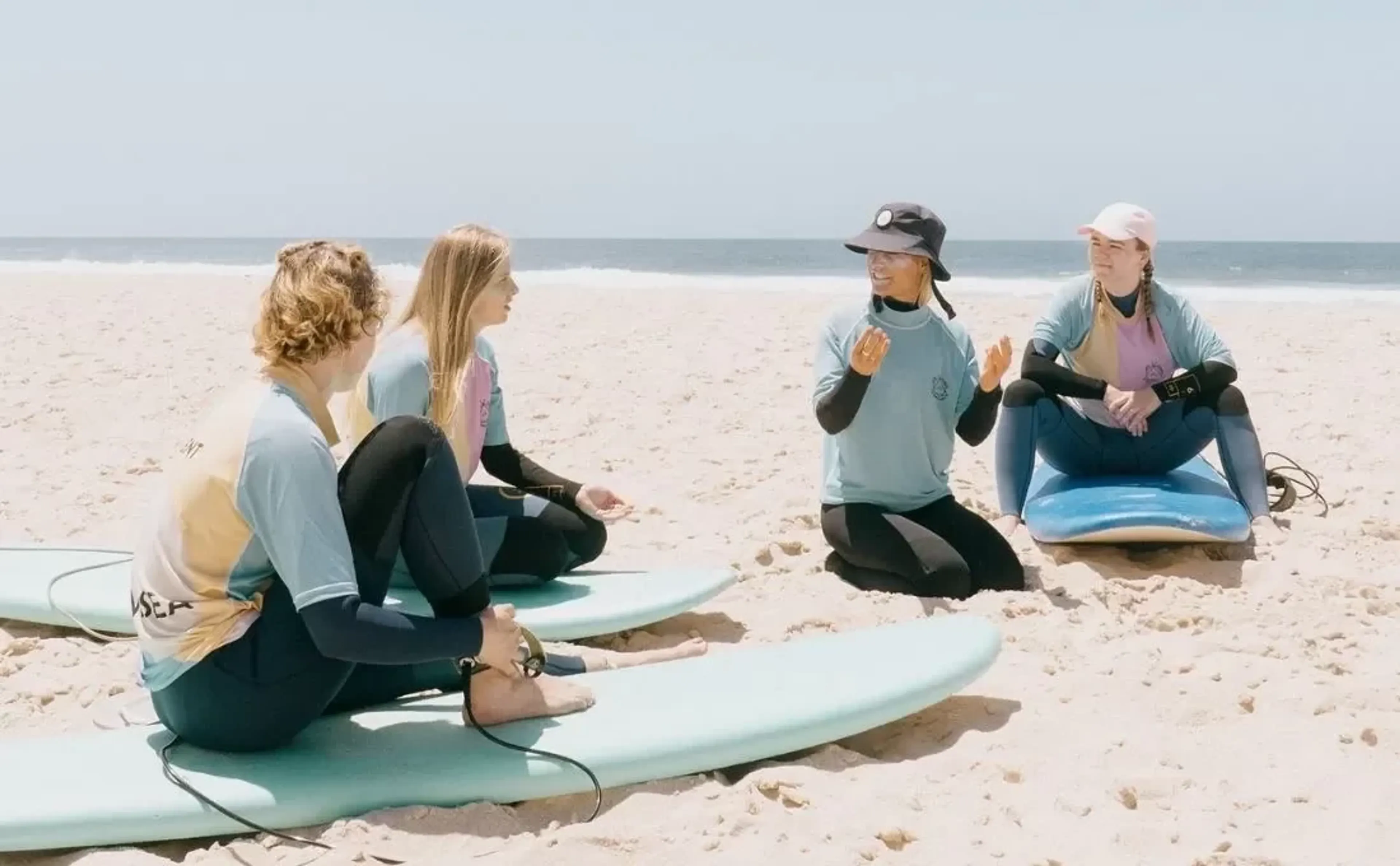 Surflehrerin erklärt Surfcamp-Gruppe Wellentheorie am Strand