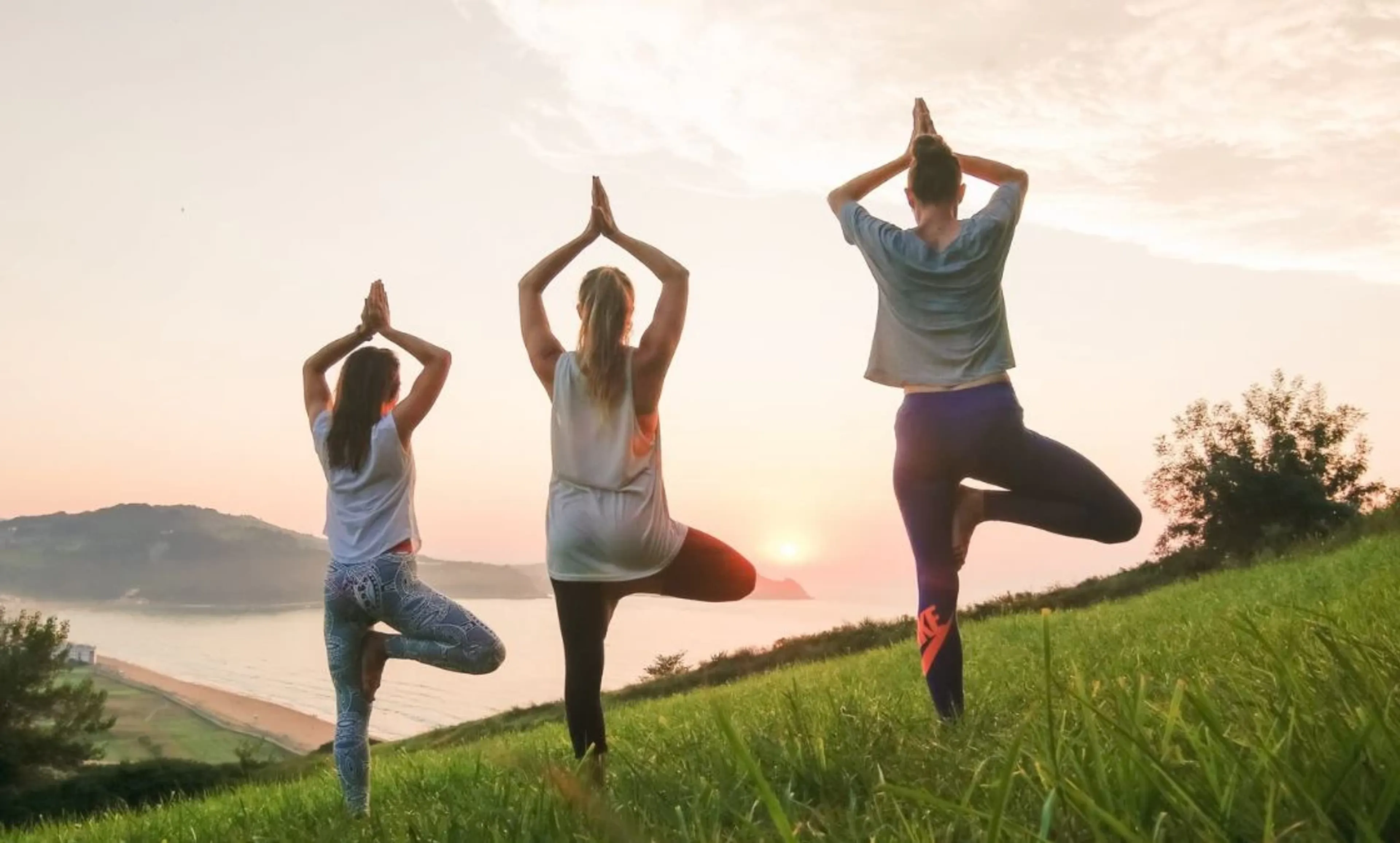 Drei Frauen beim Yoga Retreat in der Tree-Pose mit Blick aufs Meer