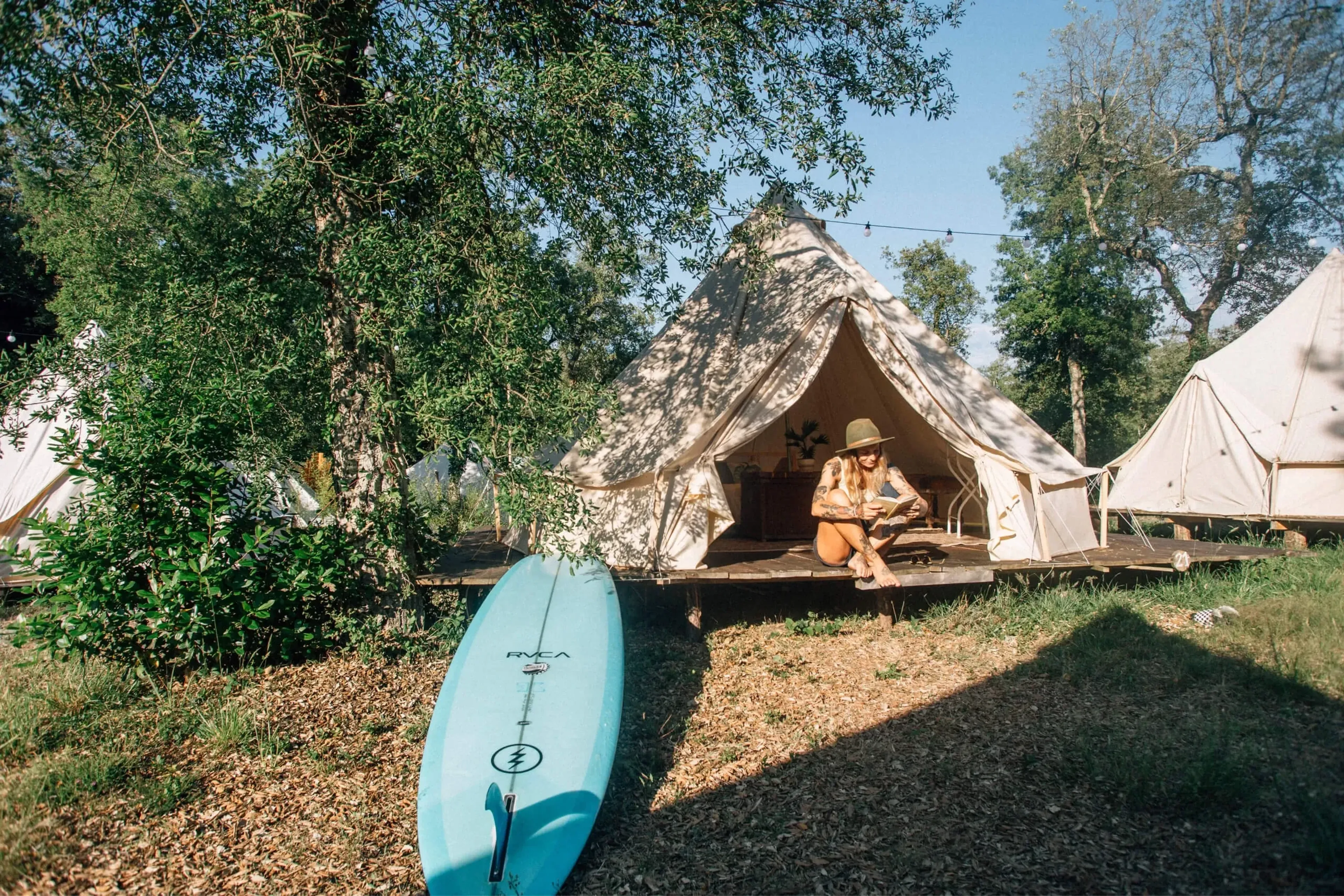 Frau sitzt im Glamping Zelt mit Surfboard