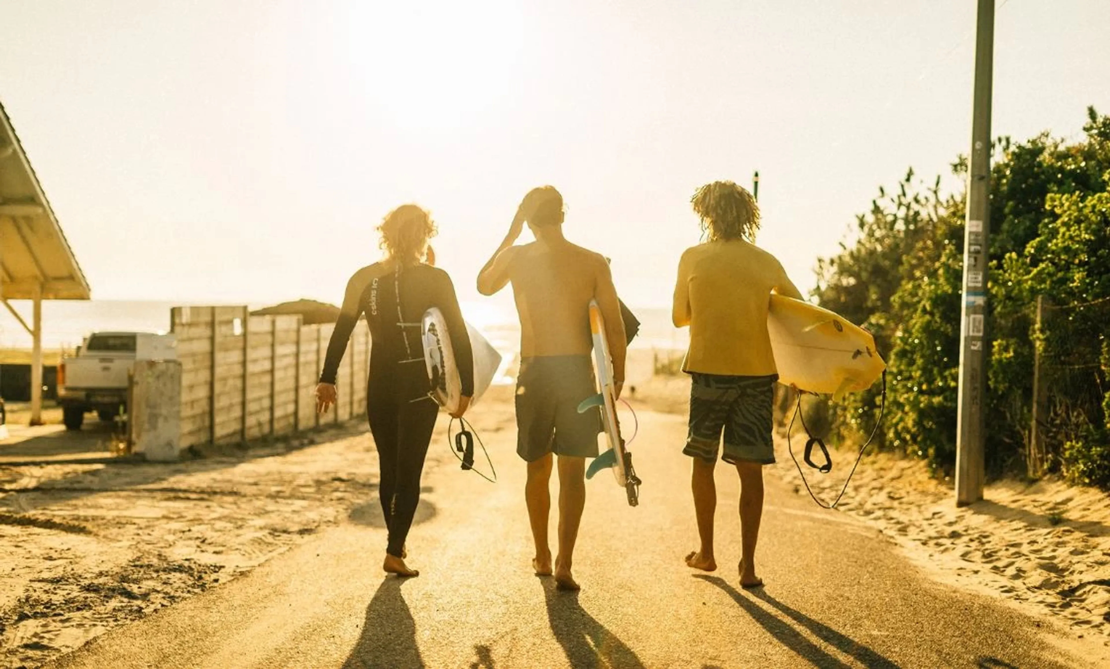 Drei Surfer laufen mit ihren Surfboards vom Surfcamp an den Strand