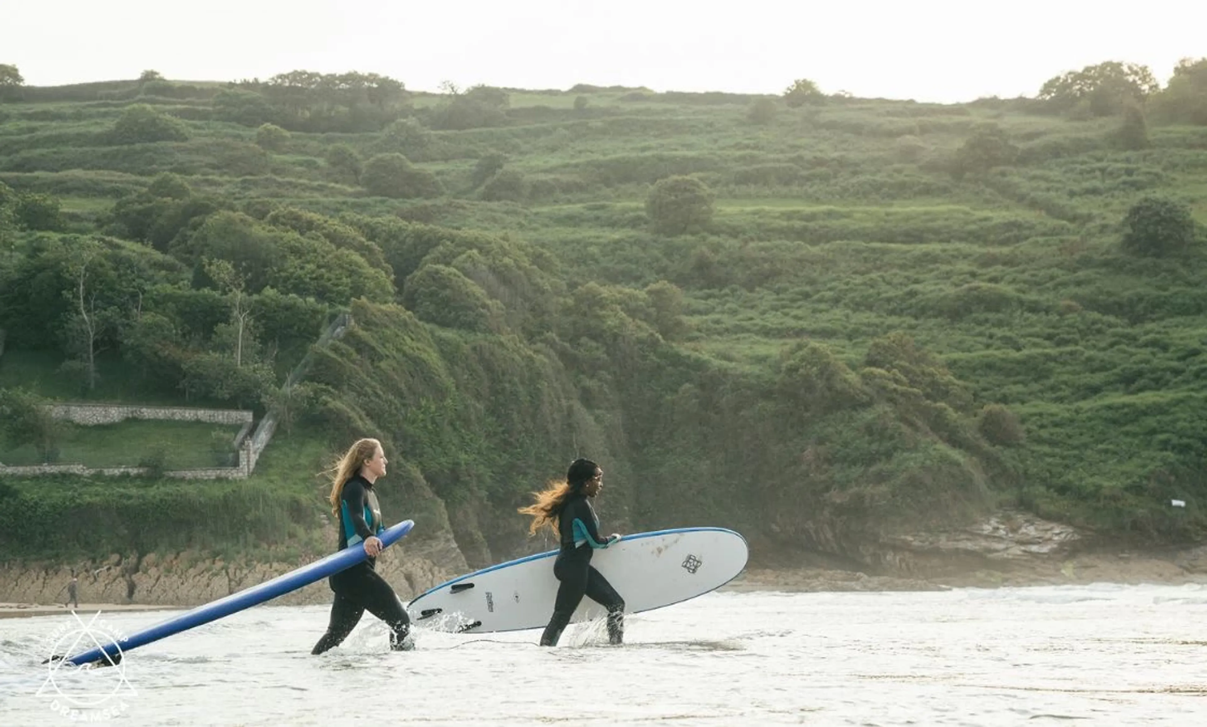 Zwei Frauen laufen mit ihrem Surfboard in die Wellen im Surfcamp in Nordspanien
