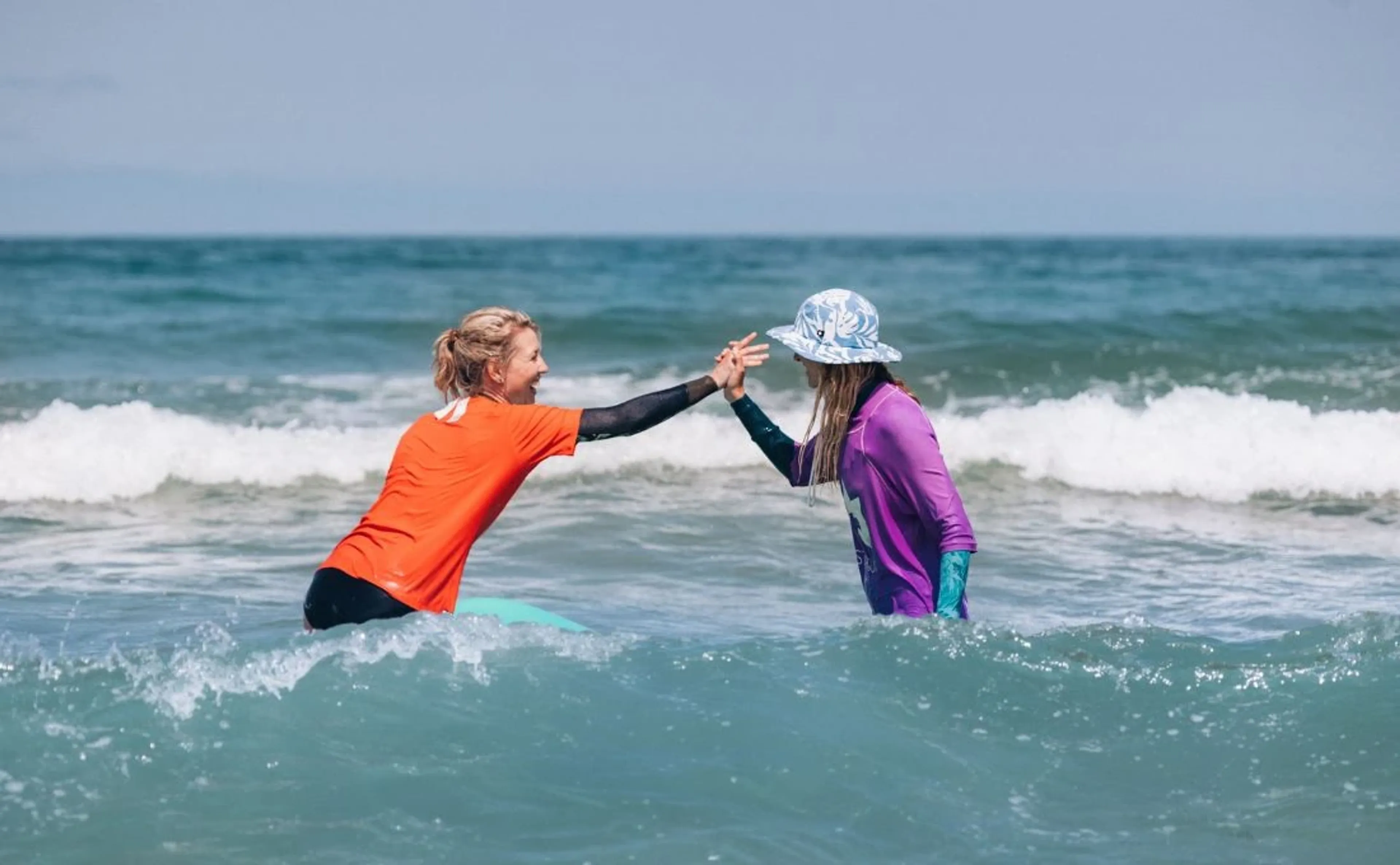 Zwei Frauen geben sich beim surfen ein High-Five