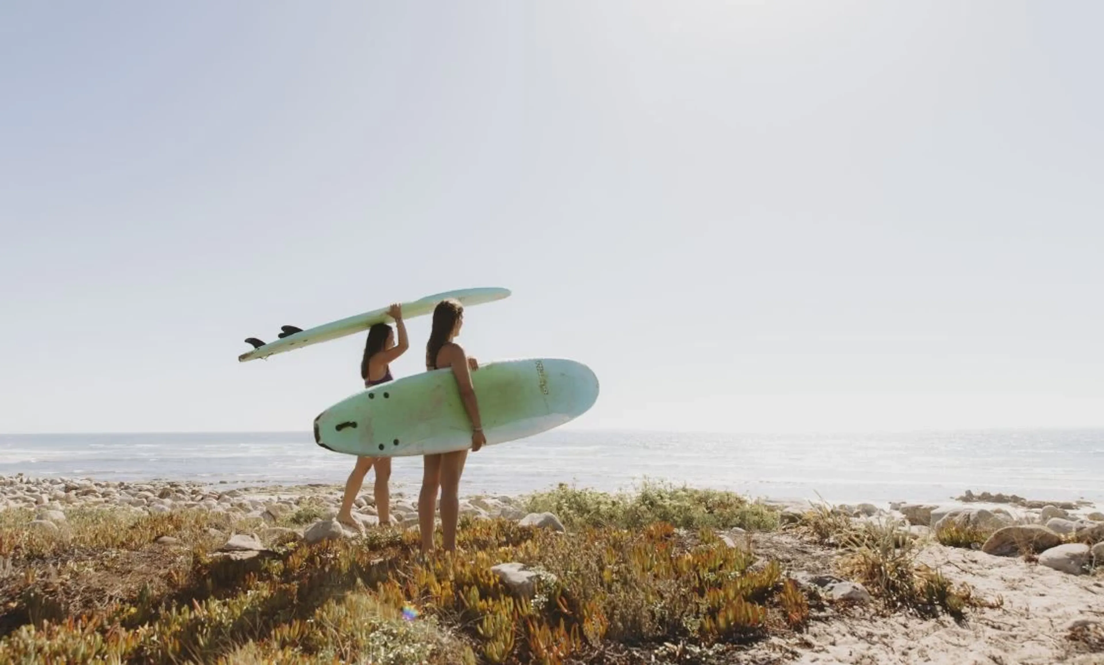 Zwei Surfer mit Surfboards beobachten die Wellen von der Düne im Alentejo in Portugal