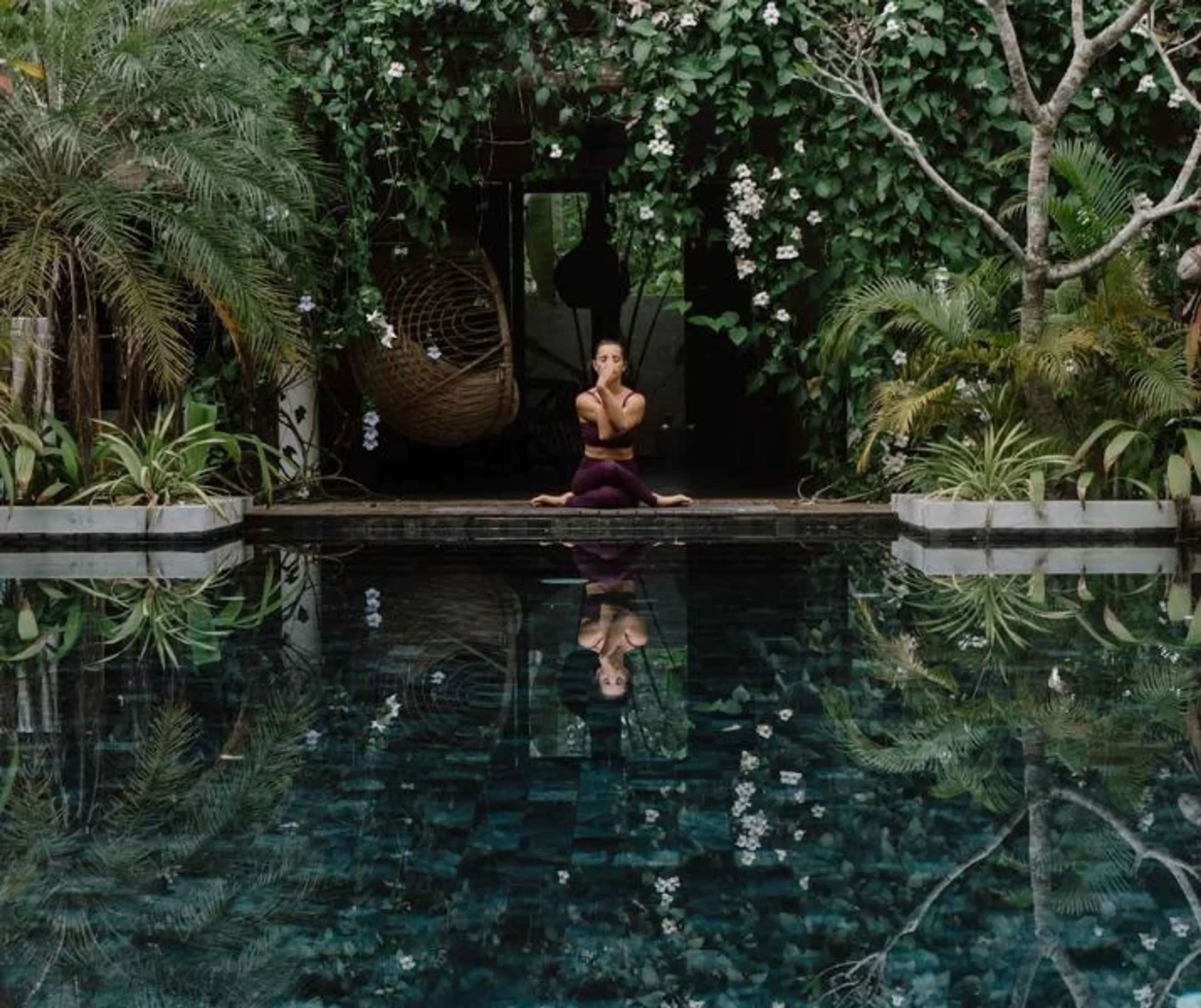 Yoga Retreat in tropischer Umgebung – Frau meditiert am Pool