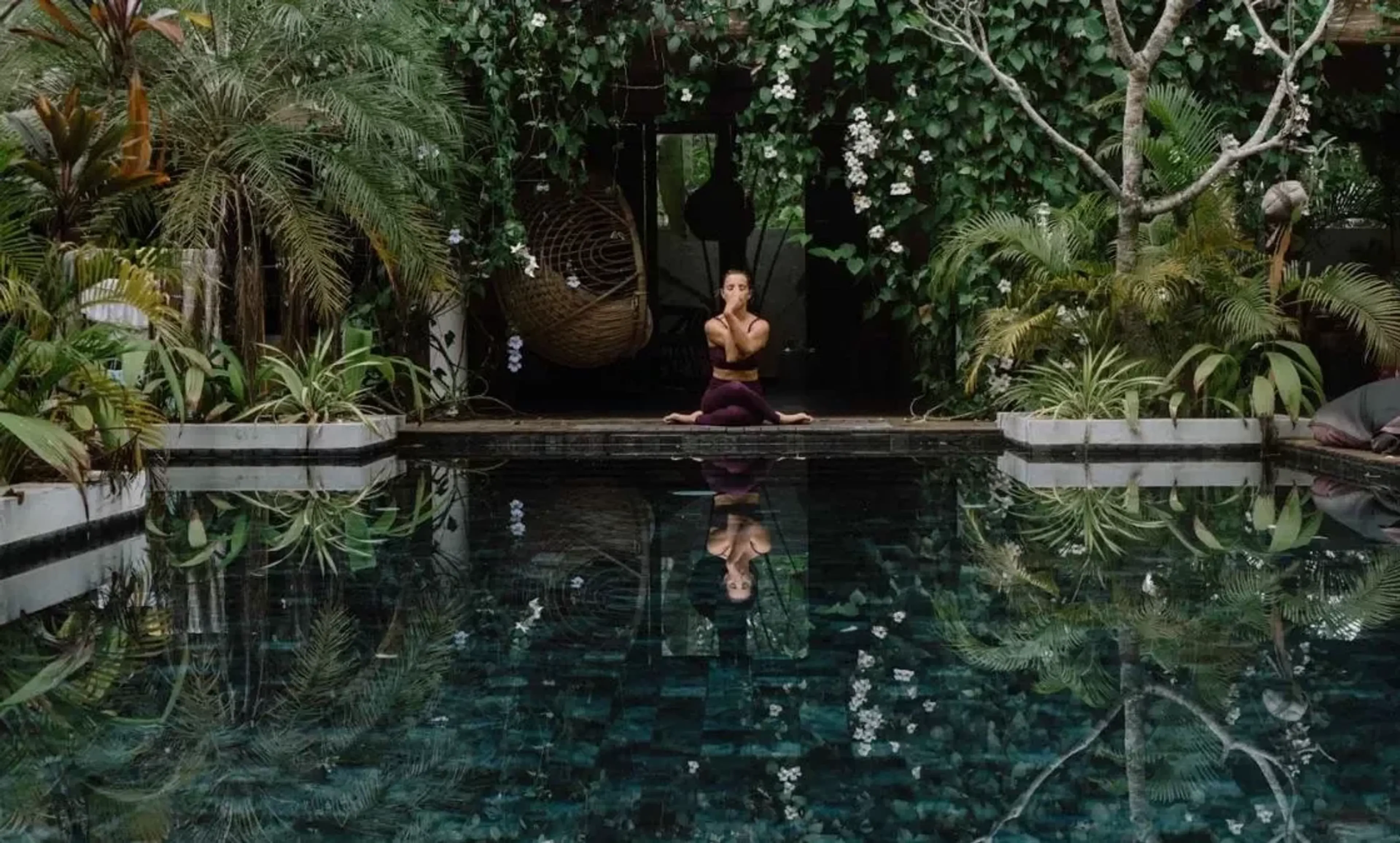 Yoga Retreat in tropischer Umgebung – Frau meditiert am Pool