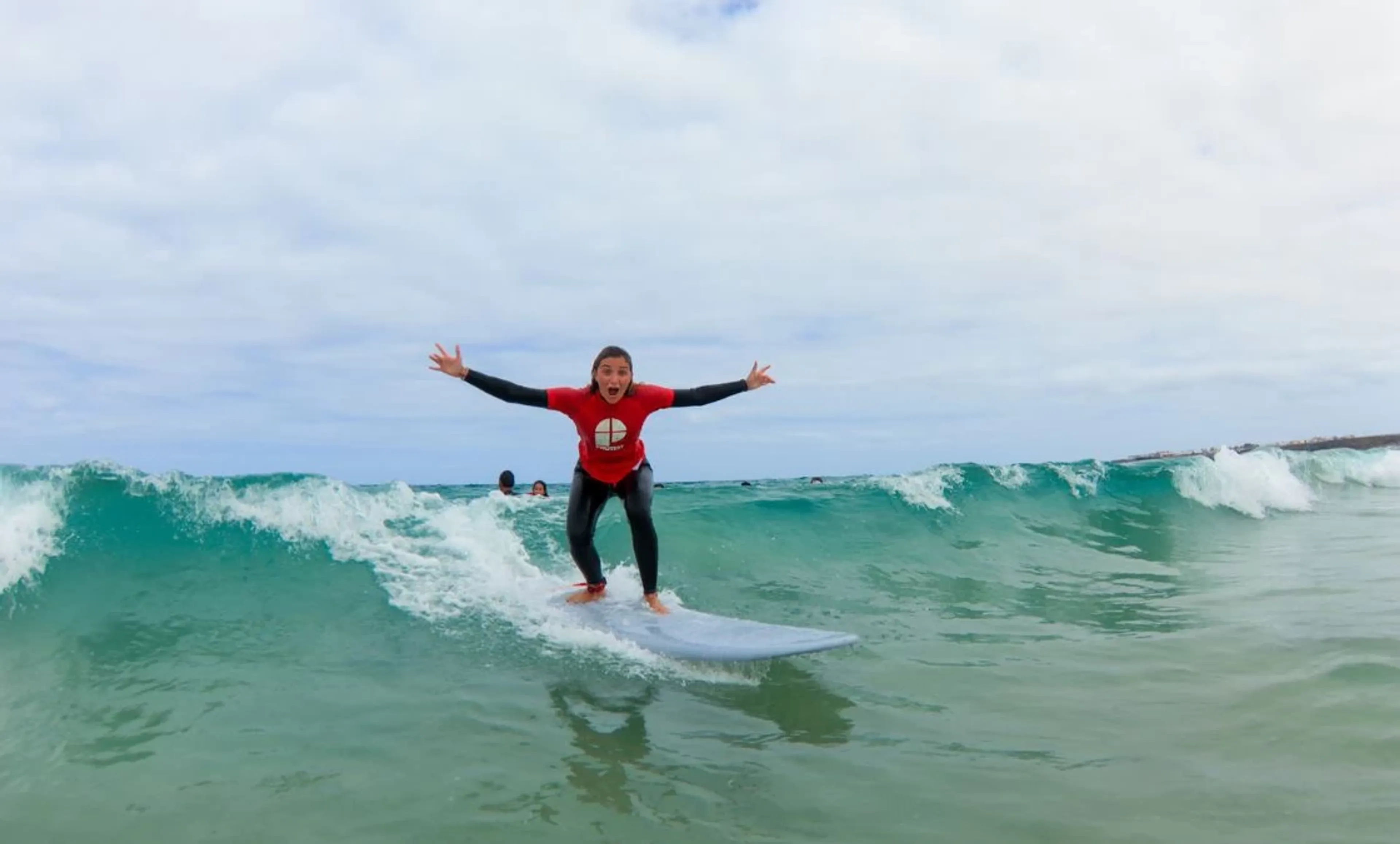 Surf-Anfängerin surft Welle und feiert mit hoch gestreckten Armen