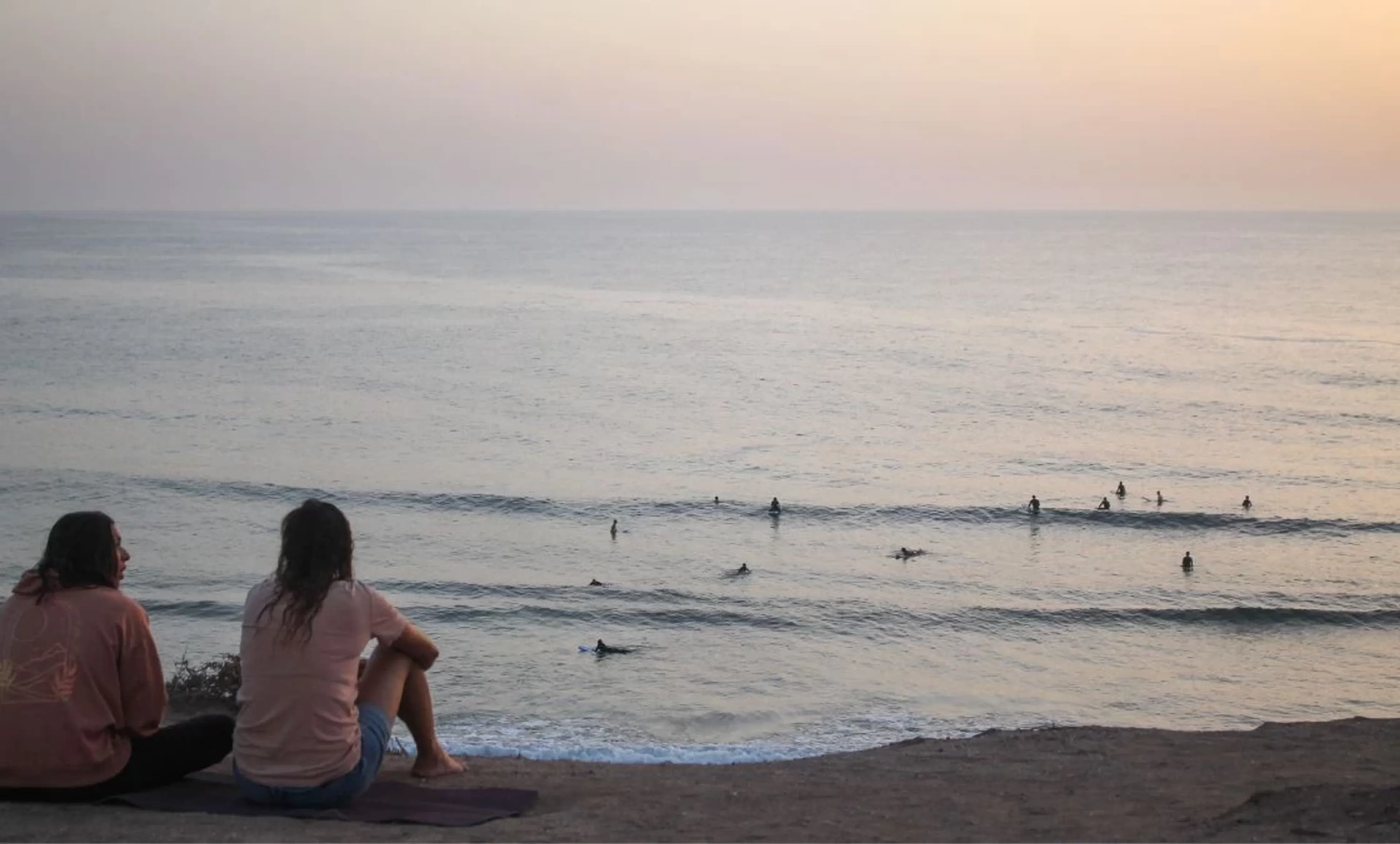 Zwei Frauen beobachten das Line-Up mit Surfern bei Sonnenuntergang