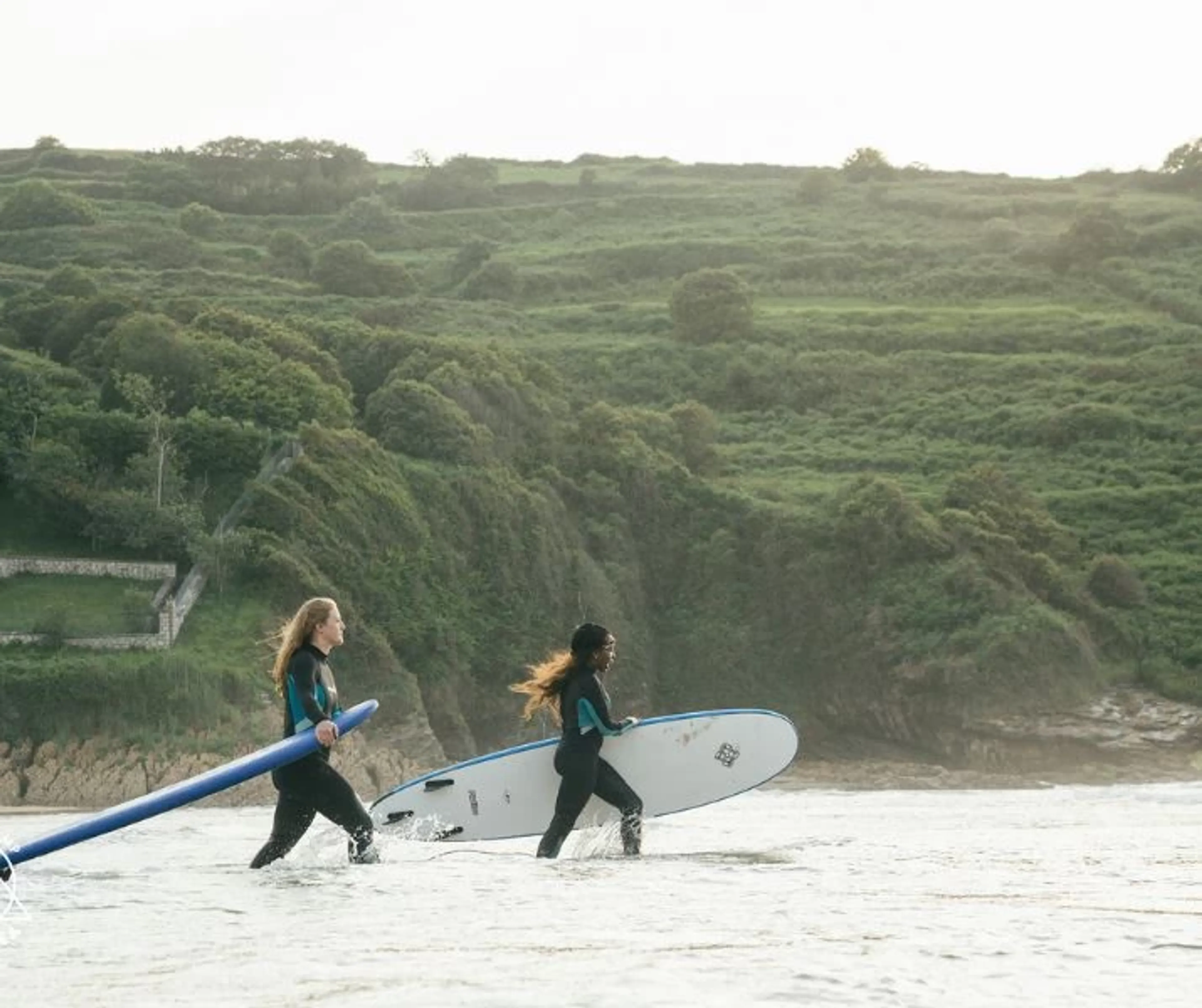 Zwei Frauen laufen mit ihrem Surfboard in die Wellen im Surfcamp in Nordspanien