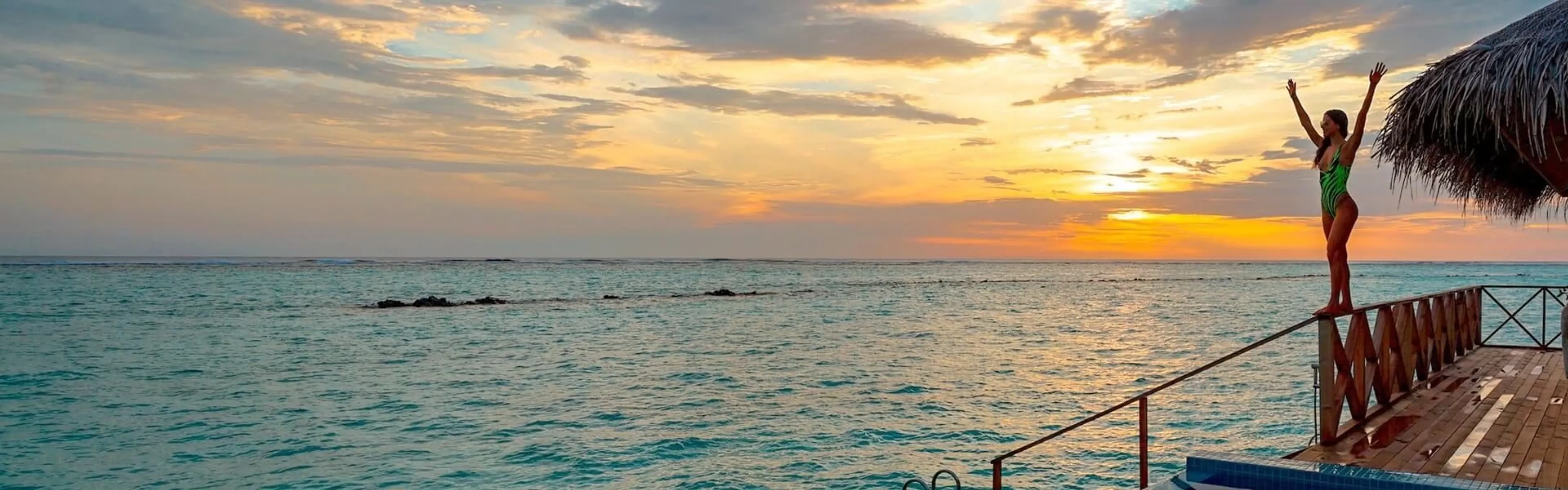 Frau mit hochgestreckten Armen bei Sonnenaufgang am Meer