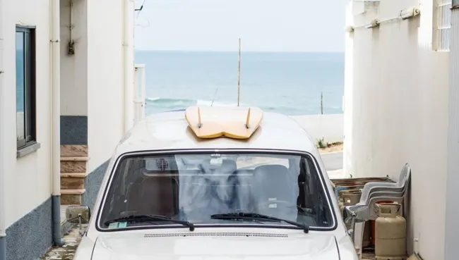 Altes Auto mit Surfboard auf dem Dach parkt mit Blick auf die Wellen in den Gassen in Ericeira