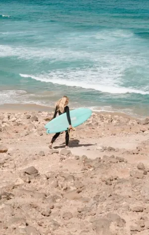 Frau läuft mit Surfboard zum Surfspot auf Fuerteventura