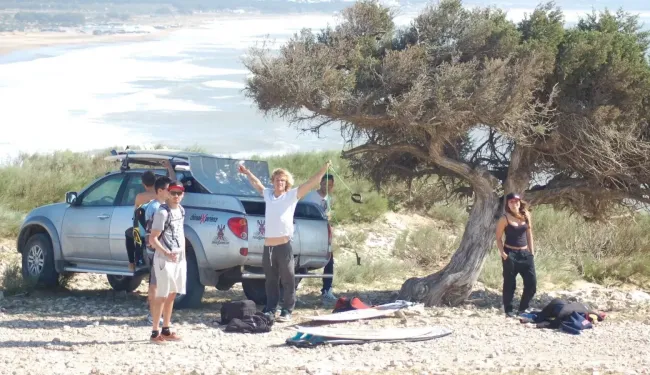 Eine Gruppe an Personen steht mit einem Auto und Surfboards in der Natur in Essaouira