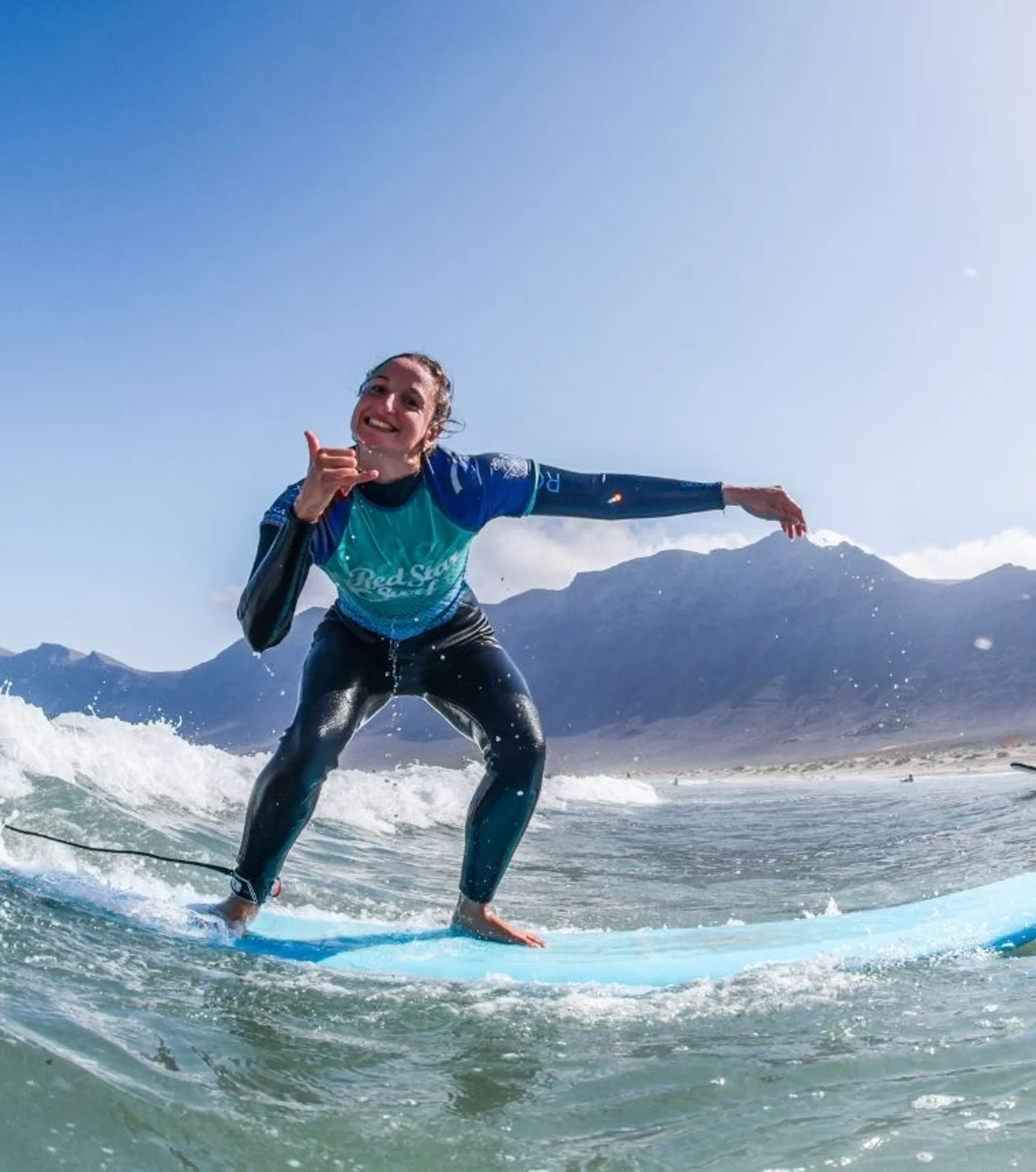 Surf-Anfängerin surft eine Weißwasserwelle auf Lanzarote und strahlt in die Kamera