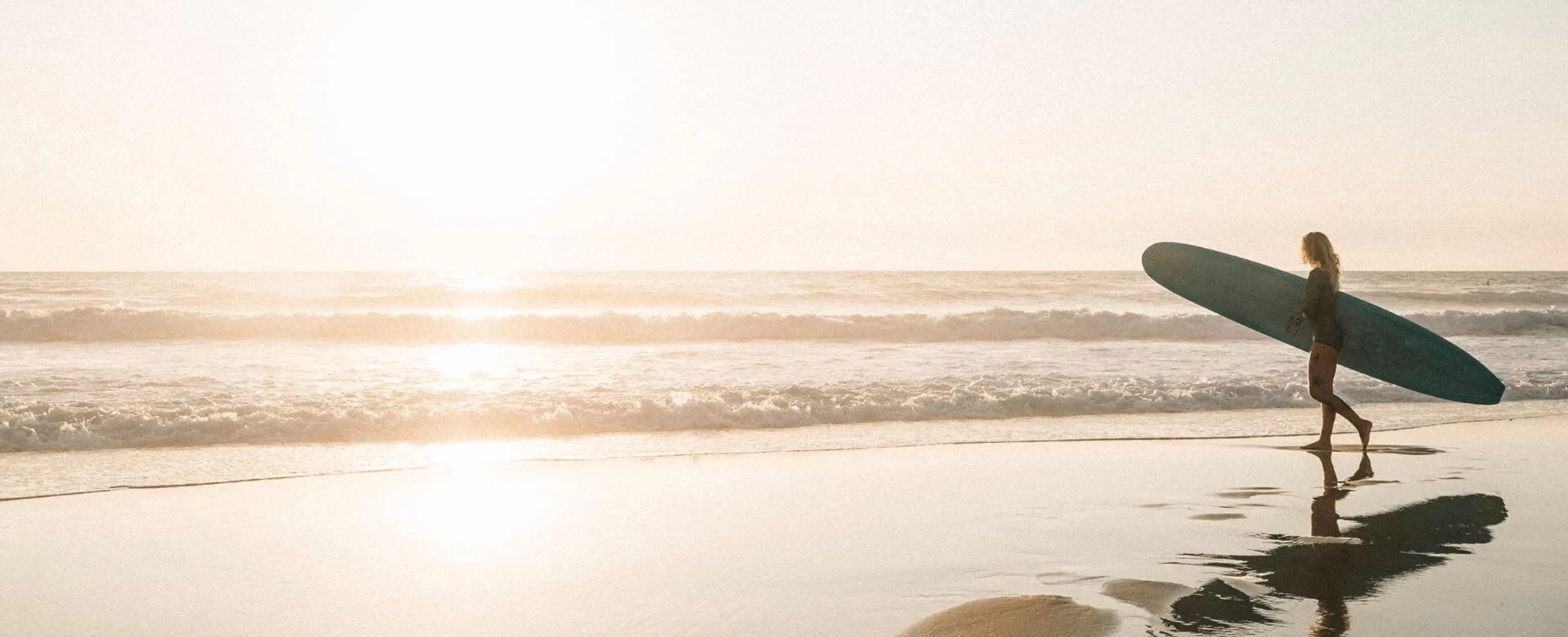 Surferin am Strand mit ihrem Surfboard bei Sonnenuntergang
