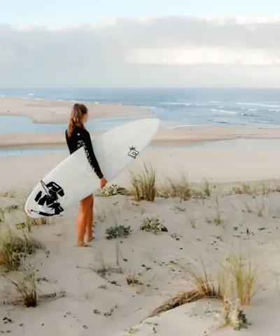 Frau mit Surfboard auf der Düne mit Blick auf die Wellen in Frankreich