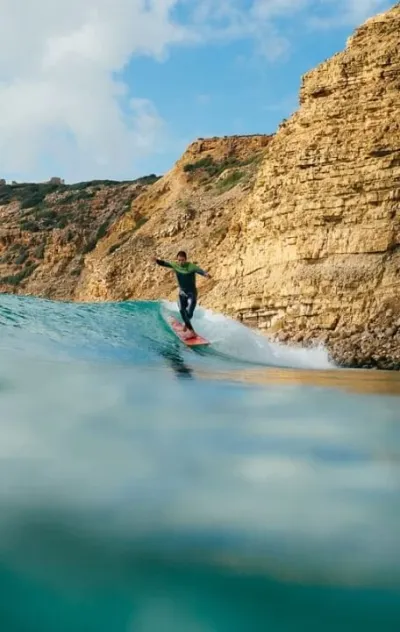 Mann surft Welle vor Klippen an der Algarve in Portugal