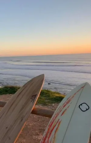 Blick vom Strand in El Palmar auf die Wellen mit Surfboards im Vordergrund und Sonnenuntergang im Hintergrund