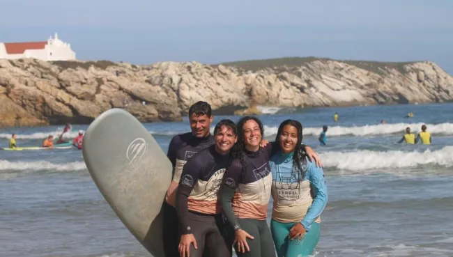 Drei Surfschüler mit ihrer Surflehrerin nach der Surf-Einheit am Strand in Baleal
