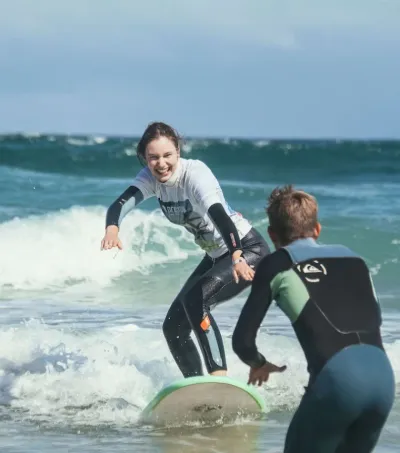 Surf-Anfängerin surft Weißwasser-Welle, angefeuert vom Surflehrer