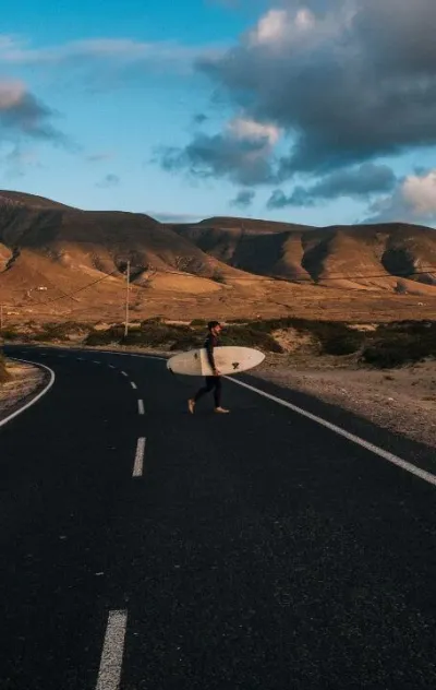 Surfer läuft mit seinem Surfboard über die Straße zum Strand auf Lanzarote