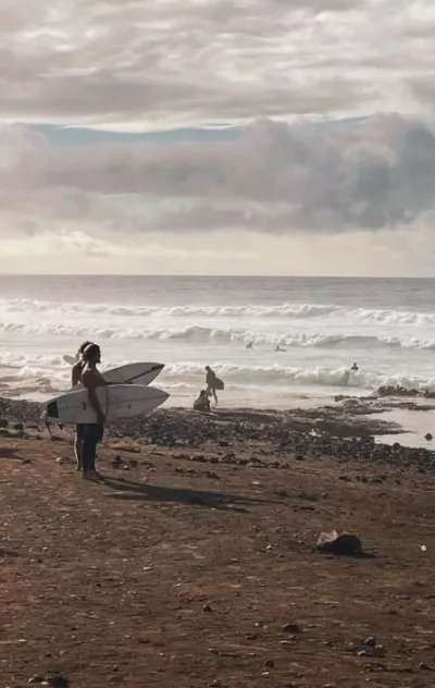 Zwei Surfer stehen mit ihren Surfboards am Strand auf Teneriffa und schauen auf die Wellen