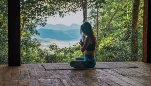 Frau meditiert auf Yoga Plattform mit Blick in die Natur