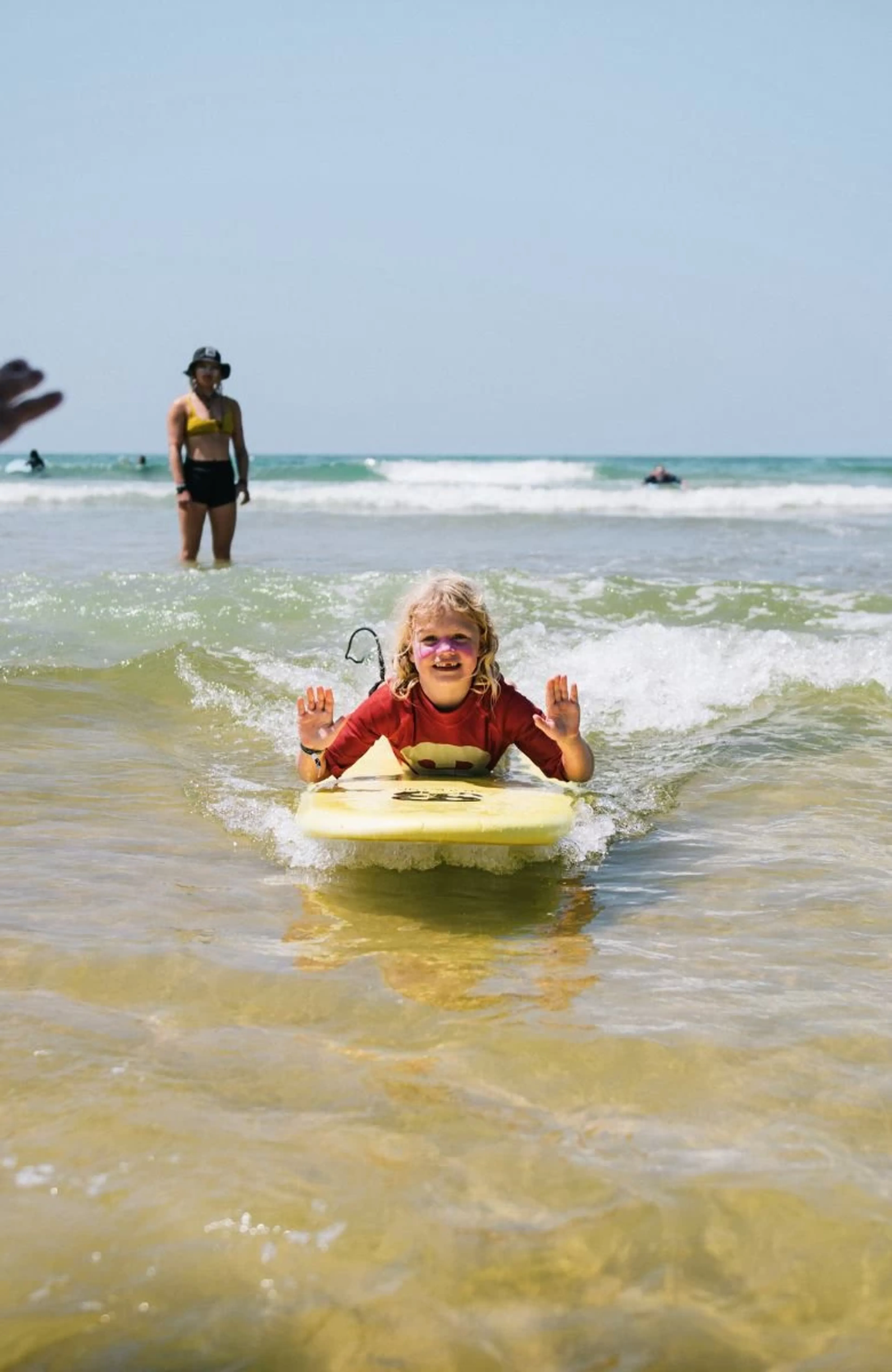 Kind liegt auf einem Surfboard und lässt sich von der Welle an den Strand bringen