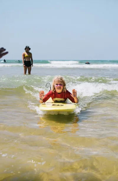 Kind liegt auf einem Surfboard und lässt sich von der Welle an den Strand bringen