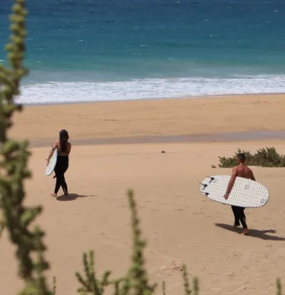 Mann und Frau laufen mit Surfboards unter dem Arm vom Surfcamp zum Strand auf Fuerteventura
