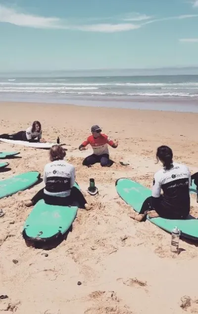 Surflehrer erklärt Surfcamp-Gruppe die Technik am Strand an der Algarve