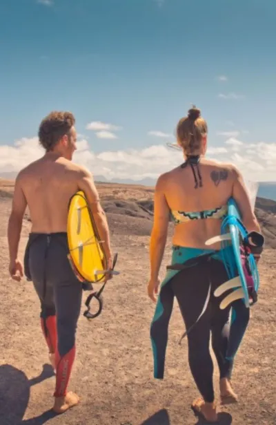 Paar läuft mit ihren Surfboards zum Strand auf Fuerteventura