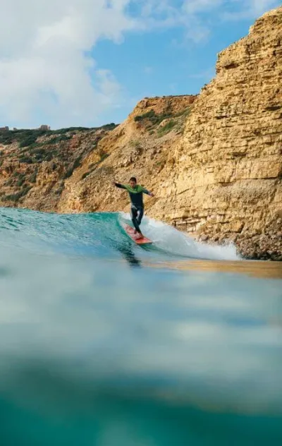 Mann surft Welle vor Klippen an der Algarve in Portugal