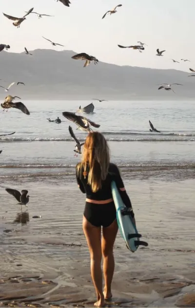 Frau läuft mit ihrem Surfboard in die Wellen in Imsouane und ist umgeben von Möwen