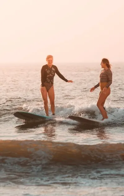 Zwei Frauen surfen gemeinsam eine Welle beim Sonnenuntergang in Lissabon