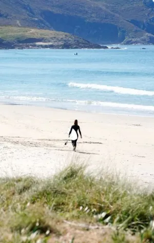Frau läuft mit ihrem Surfboard am einsamen Strand in Galicien in die Wellen