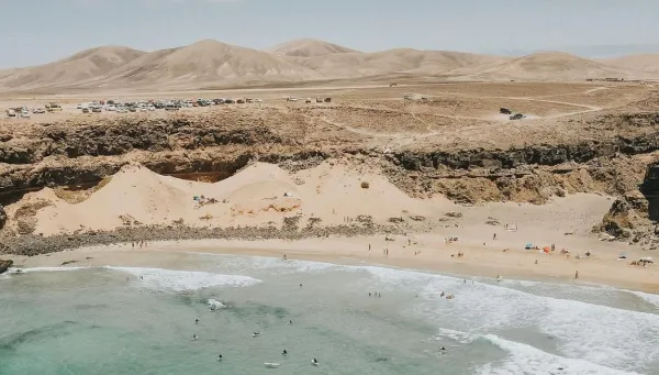 Surfcamp Gruppe im Wasser mit Blick auf die Dünen-Landschaft auf Fuerteventura