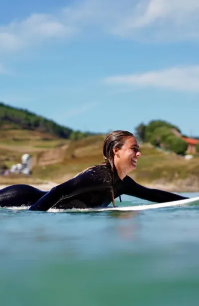 Frau paddelt mit ihrem Surfboard raus in die Wellen am Strand in Galicien