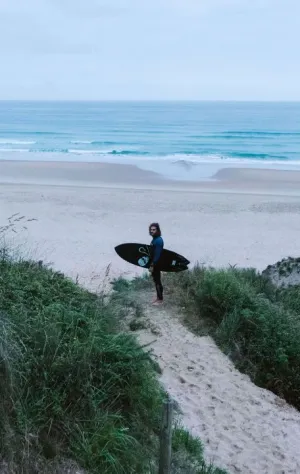 Mann mit Surfboard auf den Dünen am Strand mit Blick auf die Wellen in Kantabrien