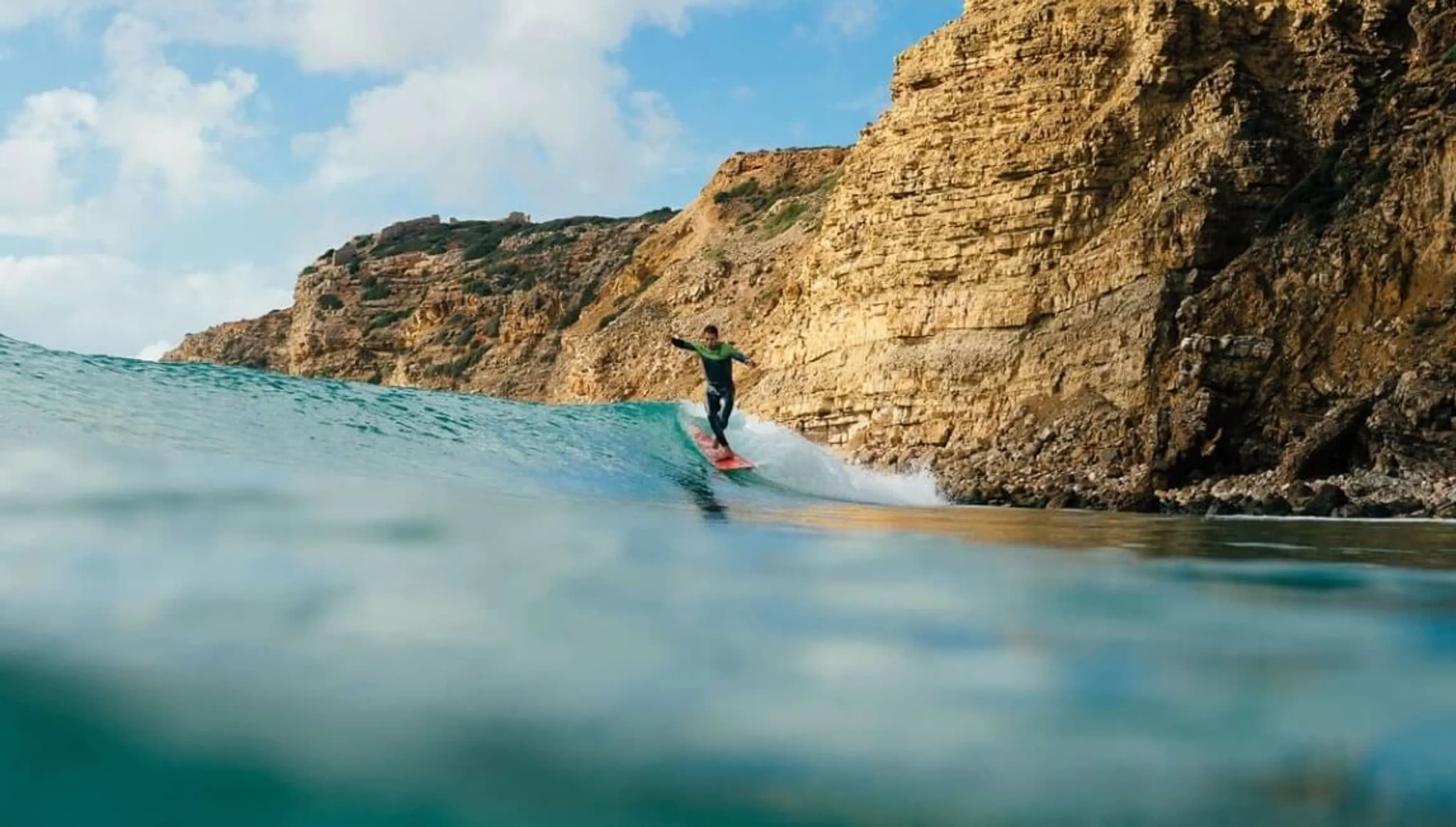 Mann surft eine Welle vor den Klippen an der Algarve