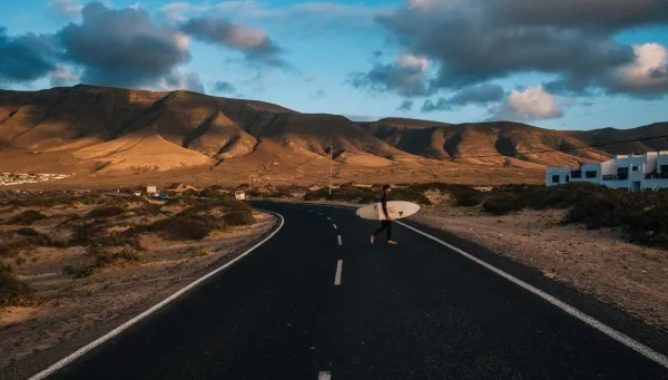 Surfer läuft mit seinem Surfbrett zum Strand vor der Bergkulisse auf Lanzarote