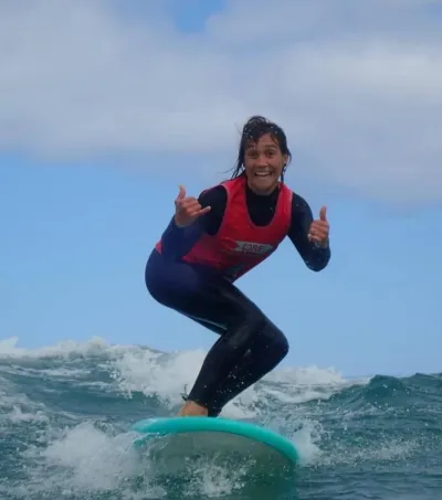 Anfängerin surft Weißwasser und zeigt dabei den Surfer-Gruß