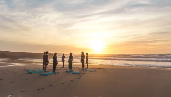 Gruppe beim Yoga am Strand bei Sonnenuntergang