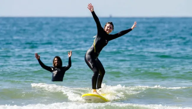Anfängerin surft in einem Surfcamp in Marokko ihre erste Welle, während ihr Surflehrer im Wasser mitfiebert