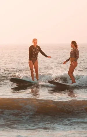 Zwei Frauen surfen zusammen eine Welle am Strand in Lissabon