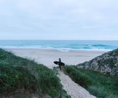 Mann mit Surfboard steht am Strand mit Blick auf die Wellen