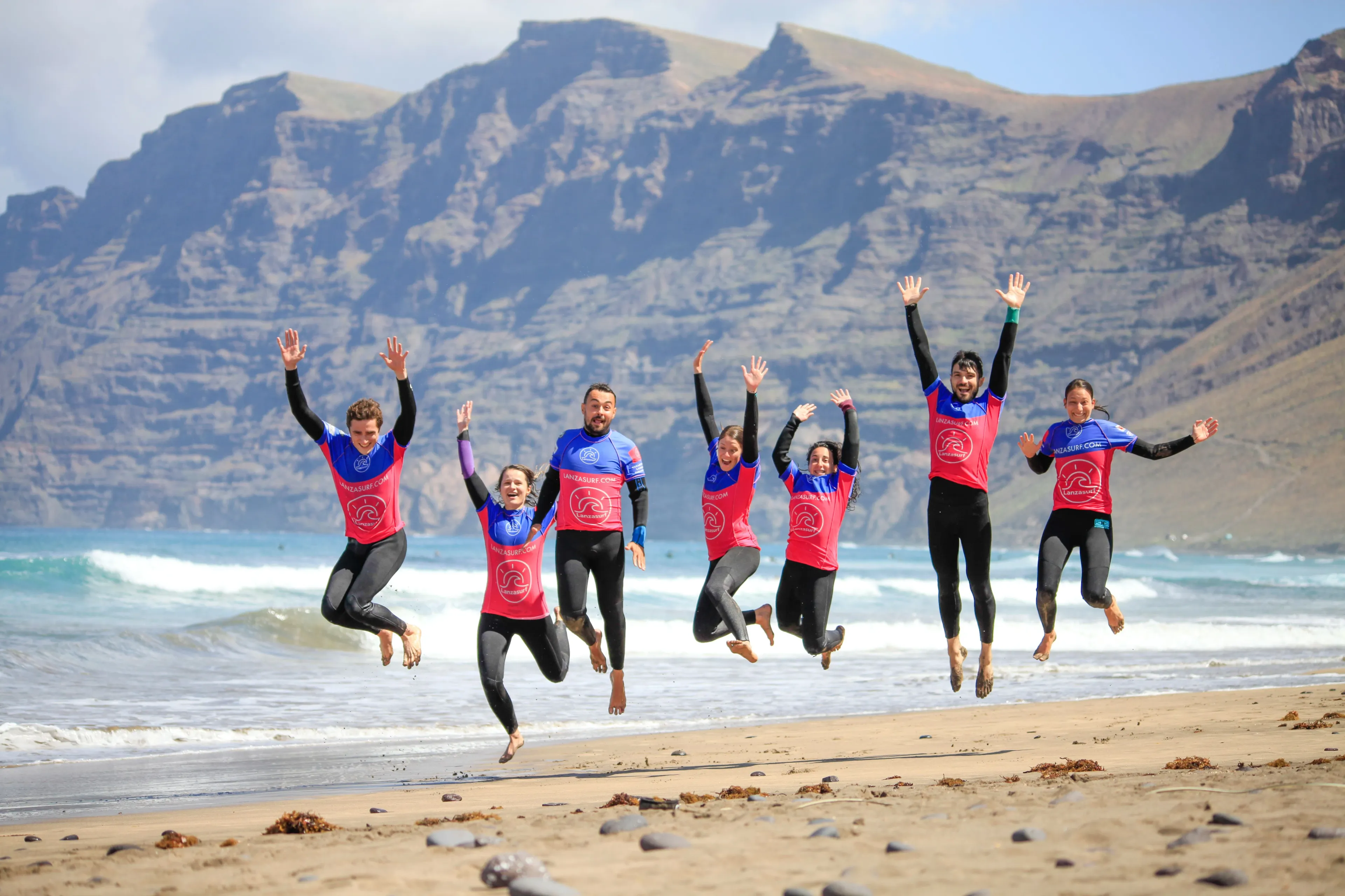 Gruppe Surfer springt fröhlich am Strand von Lanzarote