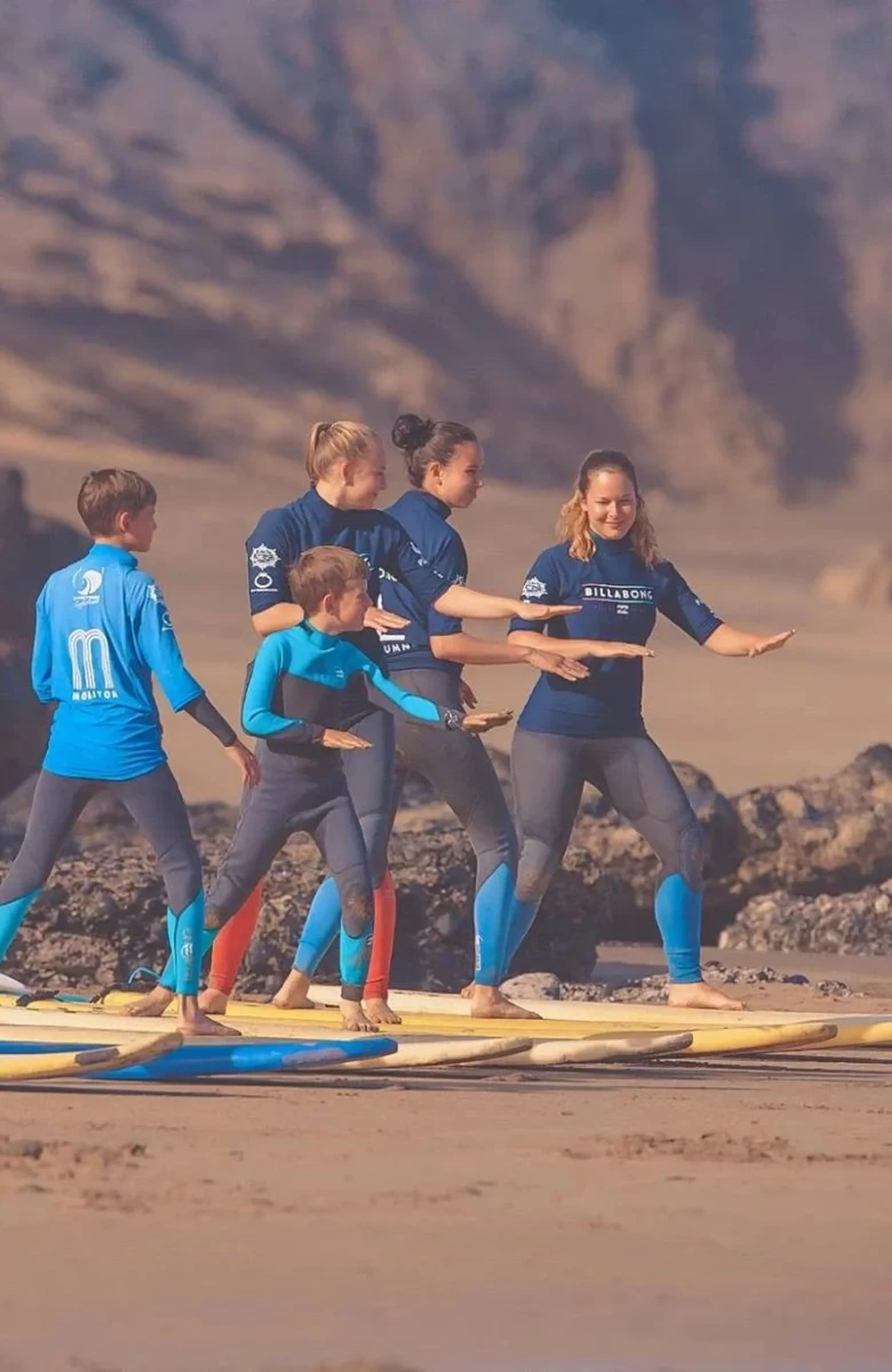 Familie übt beim Surfunterricht den Take-Off am Strand in Spanien