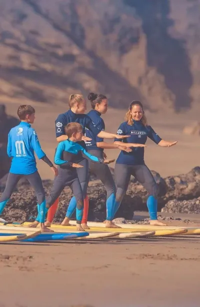 Familie übt beim Surfunterricht den Take-Off am Strand in Spanien