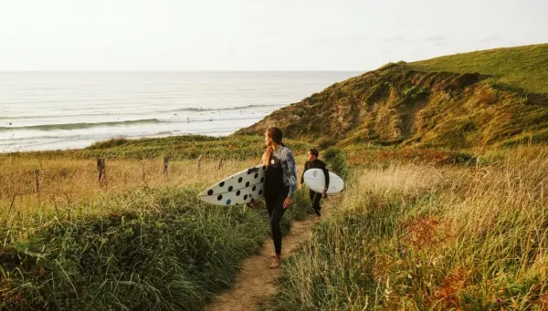 Zwei Surfer laufen mit ihren Surfboards vom Strand zurück und schauen auf die Wellen
